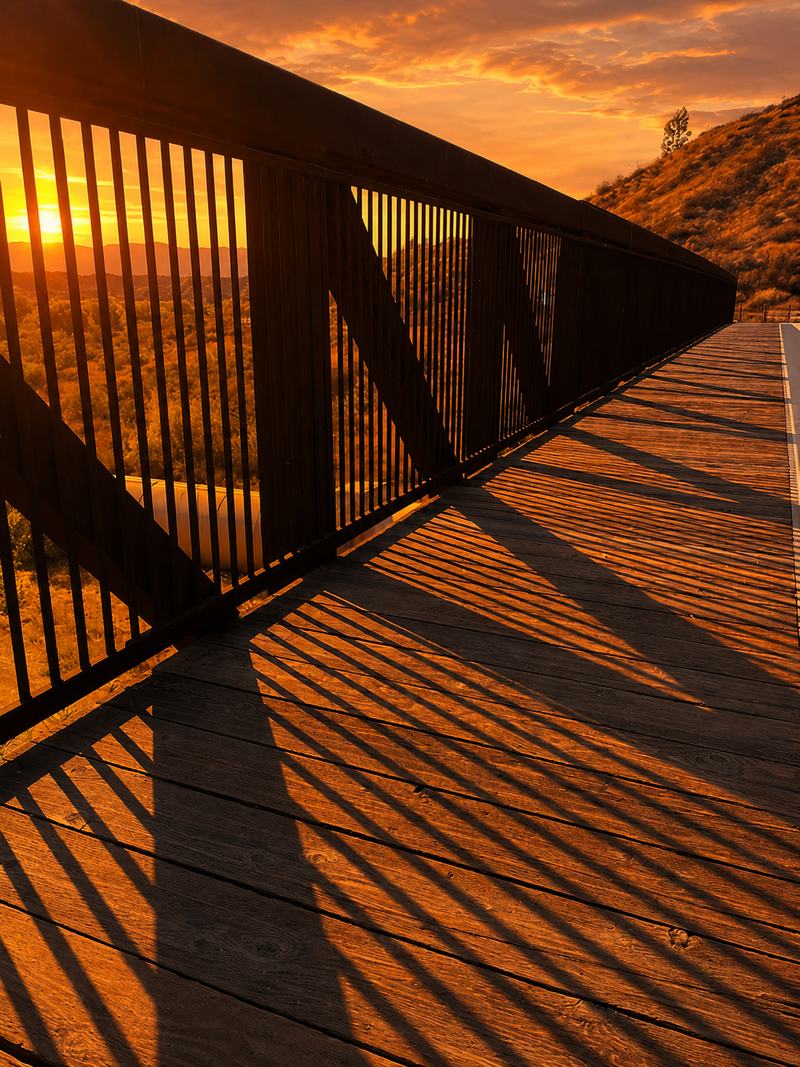 A wooden footbridge at sunset, its railings casting long shadows across the boards